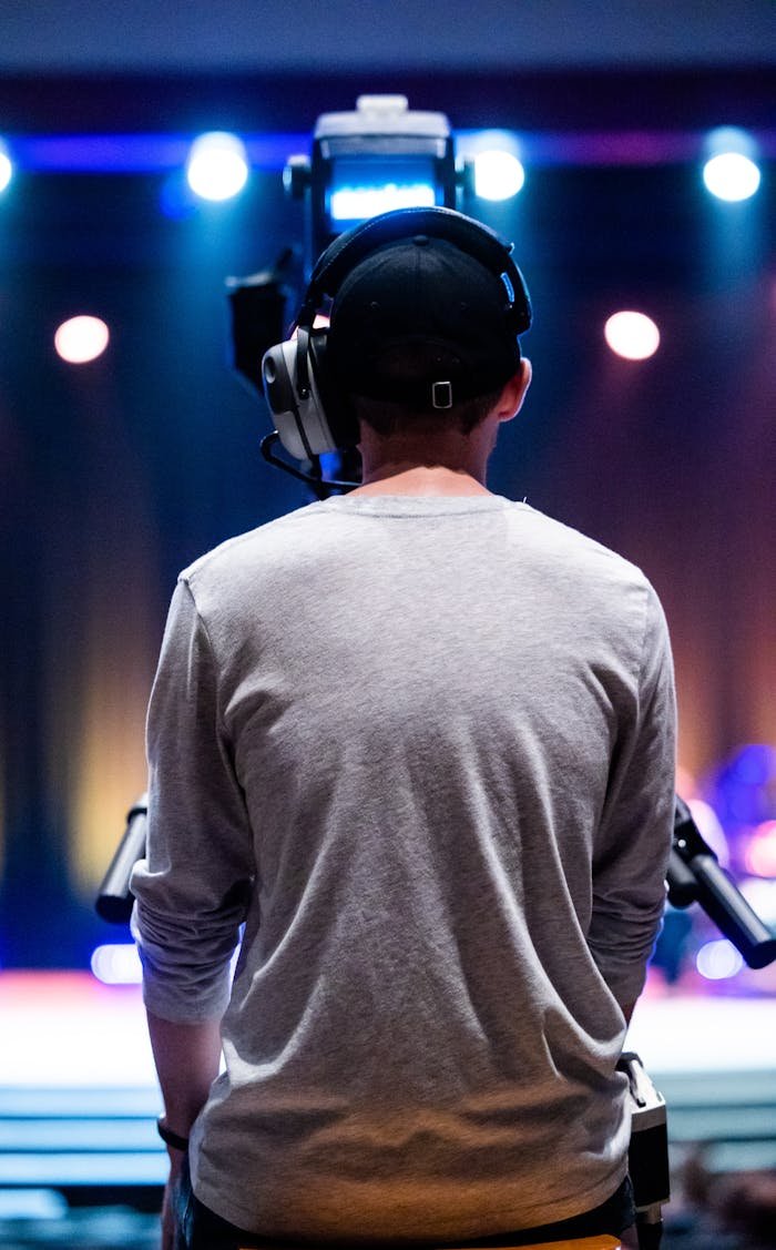 home-img Cameraman wearing headphones filming a live concert from the back. Ideal for media production themes.